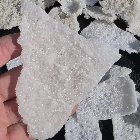 Close-up of a hand holding a piece of white crystal rock against a dark background