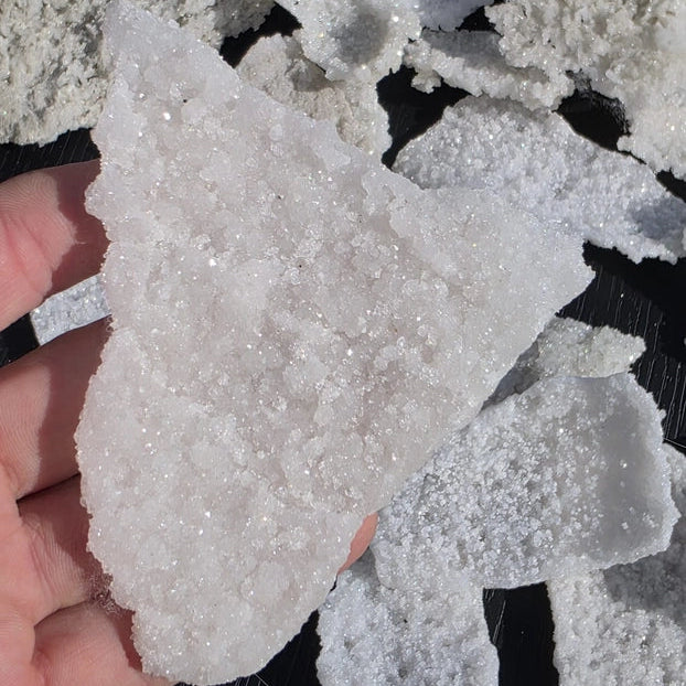 Close-up of a hand holding a piece of white crystal rock against a dark background