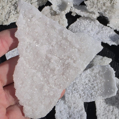 Close-up of a hand holding a piece of white crystal rock against a dark background